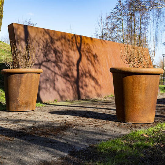 Konischer Blumenkasten aus Cortenstahl in einem Park.