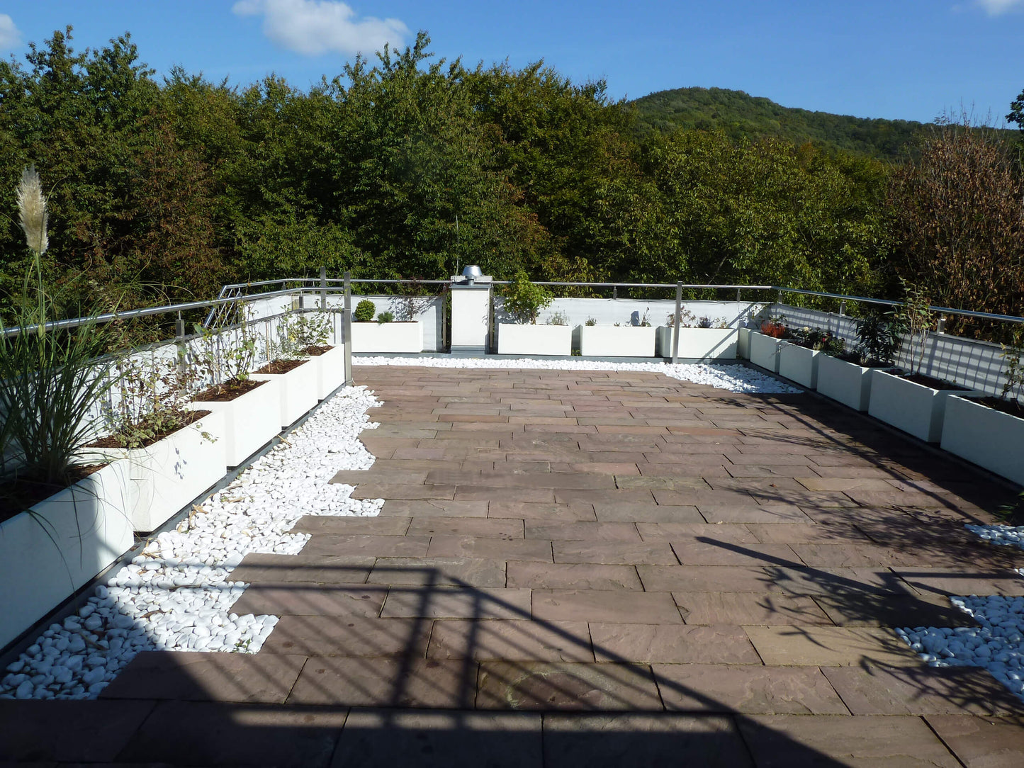 Ein weißer Blumentrog dient als Terrassenabgrenzung. Der Trog ist vielseitig einsetzbar und ermöglicht eine einfache Gestaltung der Terrassenumgebung. Sein weißes Design fügt sich harmonisch in die Umgebung ein und verleiht der Terrasse ein sauberes und modernes Aussehen.