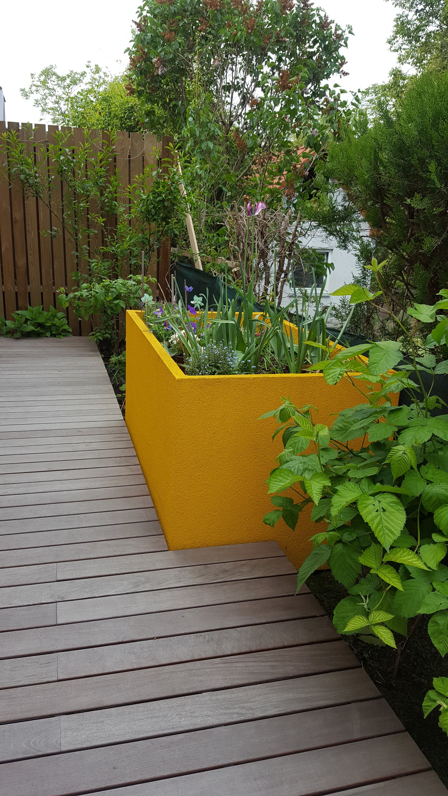 gelber mit Blumen bepflanztes hochbeet in Garten