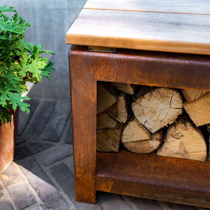 Sitzbank mit Holzlager BANCO aus Cortenstahl mit Brennholz an der Feuerstelle
