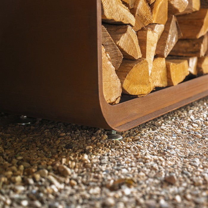 Gerundetes Holzlager CURVA aus Cortenstahl mit Bambus-Akzenten mit Brennholz im Garten